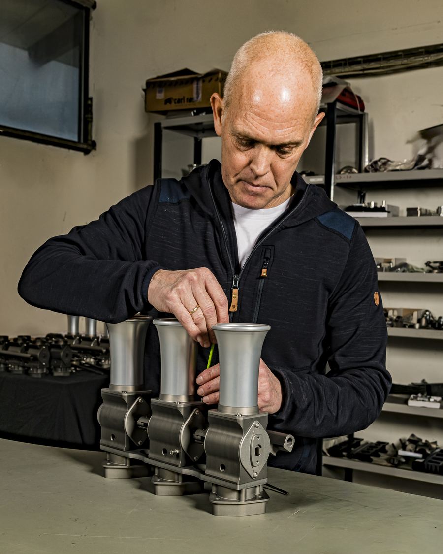 Behind the scenes at JSR Engineering in Denmark: hand-assembling a Rennen ITB throttle body bank at the workshop bench, machined components on the shelves behind